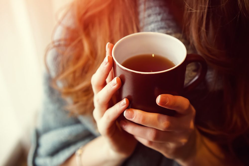 Drink Tea relax cosy photo with blurred background. Female hands holding mug of hot Tea in morning. Young woman relaxing tea cup on hand. Good morning Tea or Have a happy day message concept.