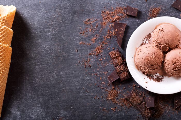 plate of ice cream scoops surrounded with chocolate next to waffle cones