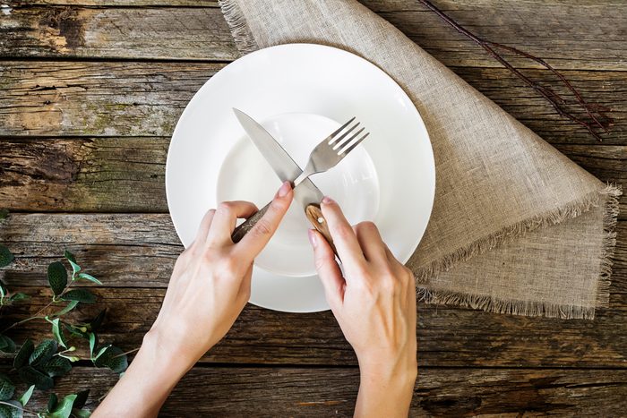 hands holding knife and fork over a plate
