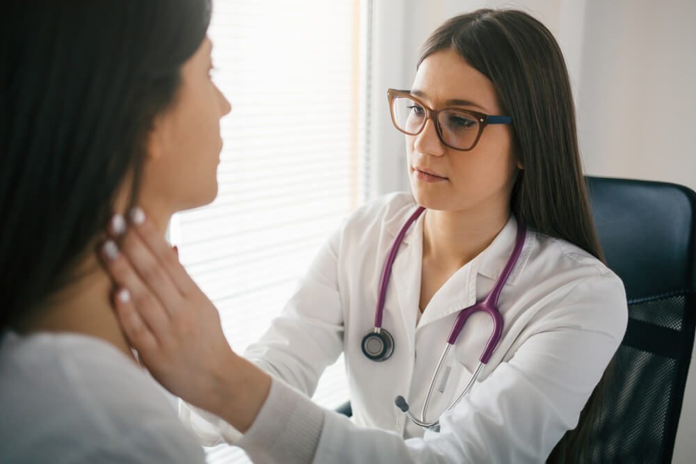 Young female doctor palpating lymph nodes of a patient. Doctor touching the throat of a patient. Medical exam, clinic, hospital