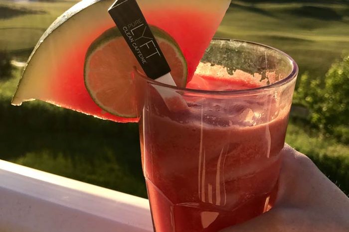 red smoothie in a clear glass with a lime wedge and slice of watermelon