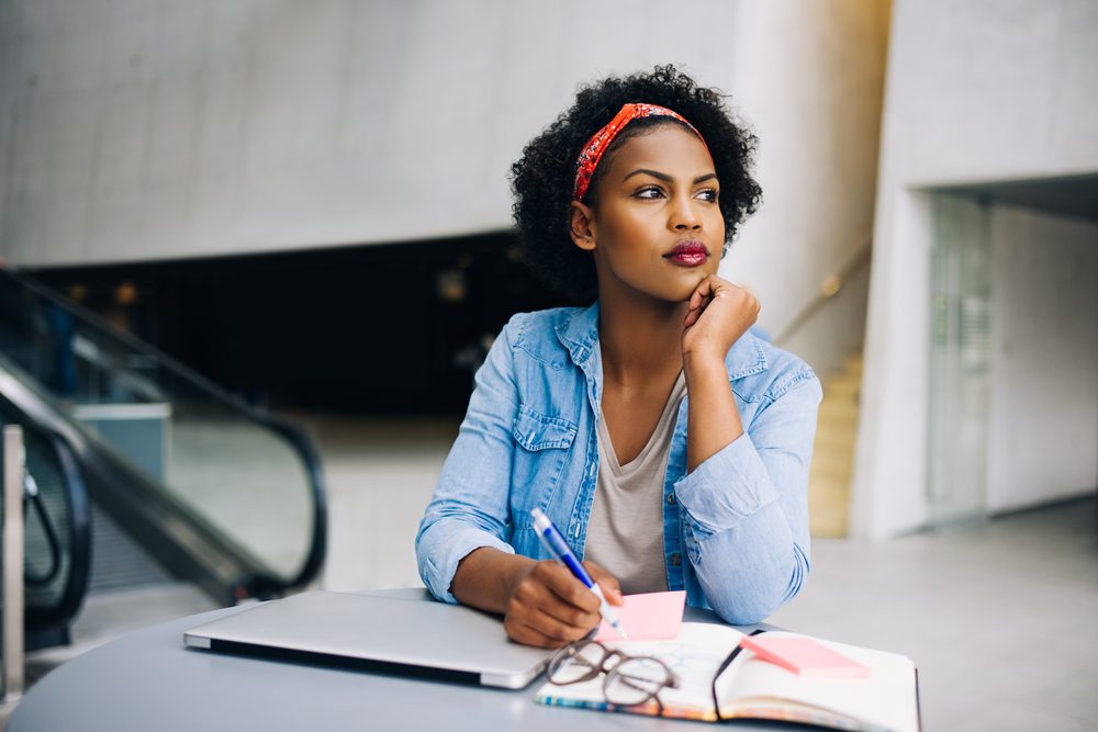 Focused young woman deep in thought while working at a table in a modern office building lobby