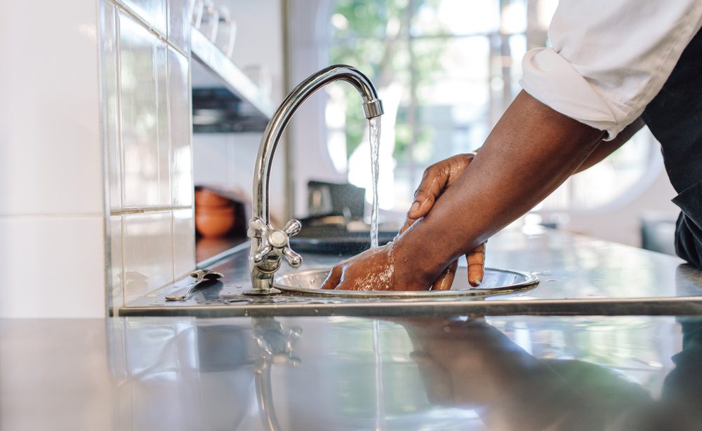 Close up of chef washing his hands in commercial kitchen. Man washing hands in a sink with tap water.