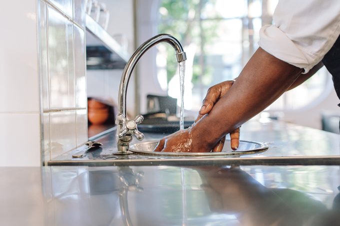 Close up of chef washing his hands in commercial kitchen. Man washing hands in a sink with tap water.