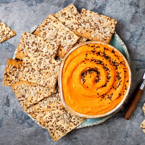 Pumpkin hummus seasoned with olive oil and black sesame seeds with whole grain crackers. Healthy vegetarian appetizer or snack 