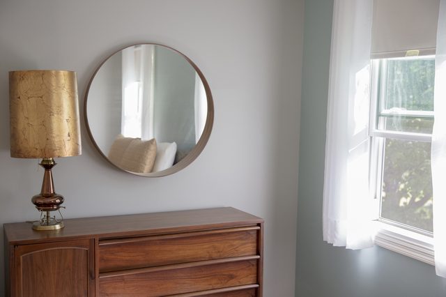 Corner of a mid-century modern bedroom with grey walls, circular mirror, a teak dresser, and a fantastic retro gold lamp.