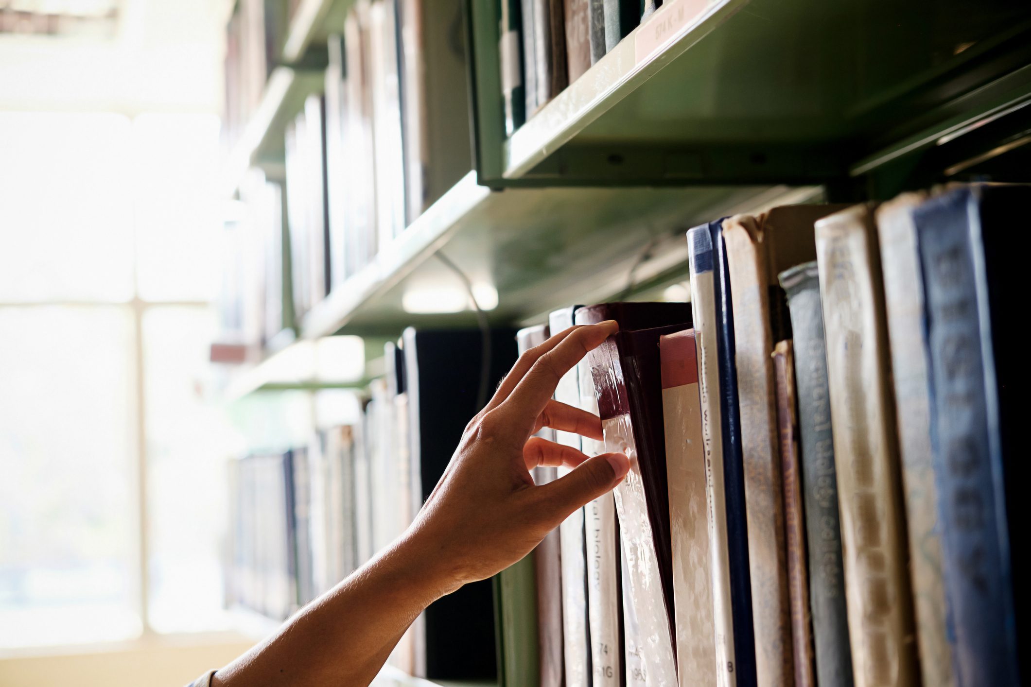 hand reaching for book on library shelf