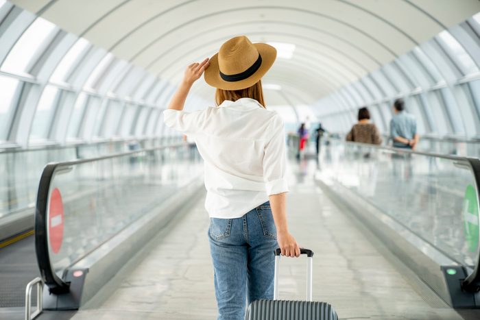 rear view of woman walking through airport holding suitcase