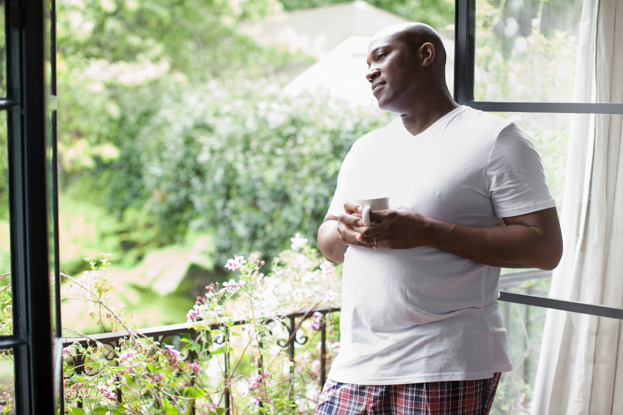 man looking out window drinking coffee in the morning