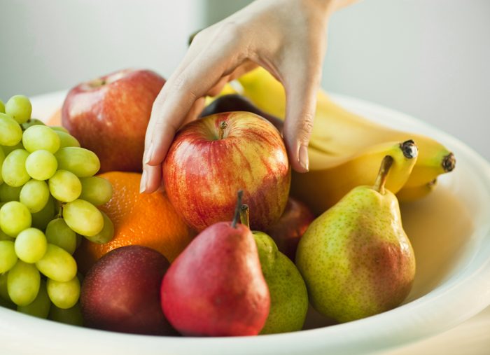 bowl of fruit close up of hand picking up red apple