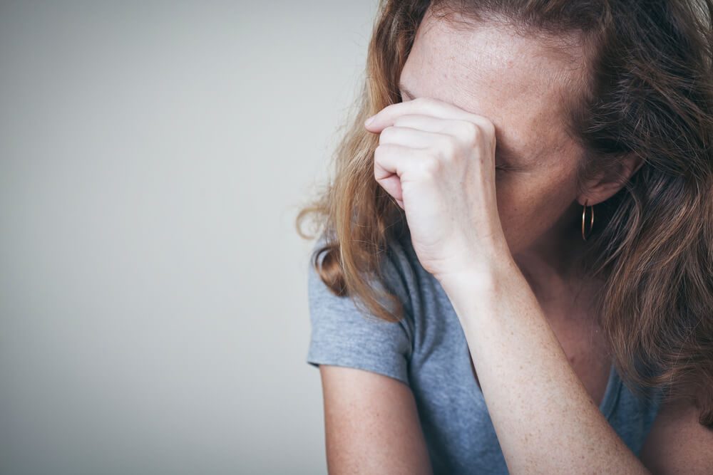 one sad woman sitting near a wall and holding her head in her hands