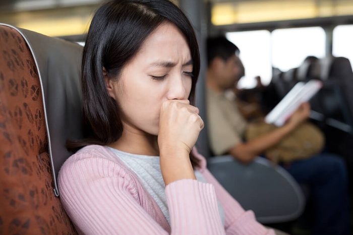 Woman coughing with hand on mouth, sitting in an airplane