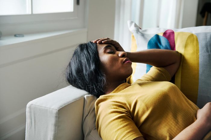 Woman lying on couch with eyes closed and hand on head