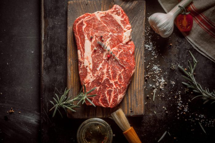 Close up Wooden Chopping Board with Raw Beef Meat on a Rustic Table with Herbs and Spices