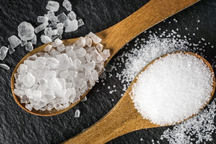 two wooden spoons filled with table and rock salt