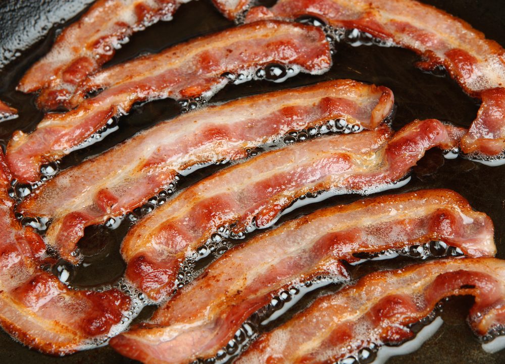 Bacon strips or rashers being cooked in frying pan.