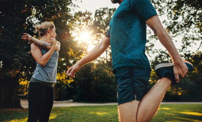 Young man and woman doing stretching exercise in the park. Young couple warming up for morning workout.