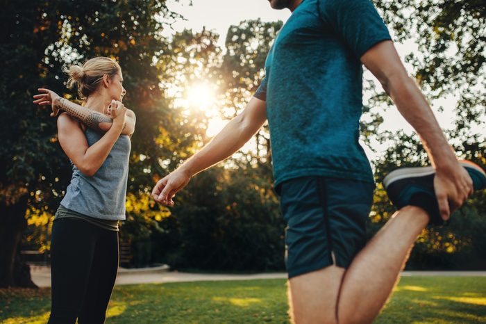 Shot of young man and woman doing stretching exercise in the park. Young couple warming up for morning workout.