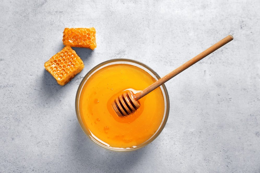 Glass bowl with delicious honey and dipper on table