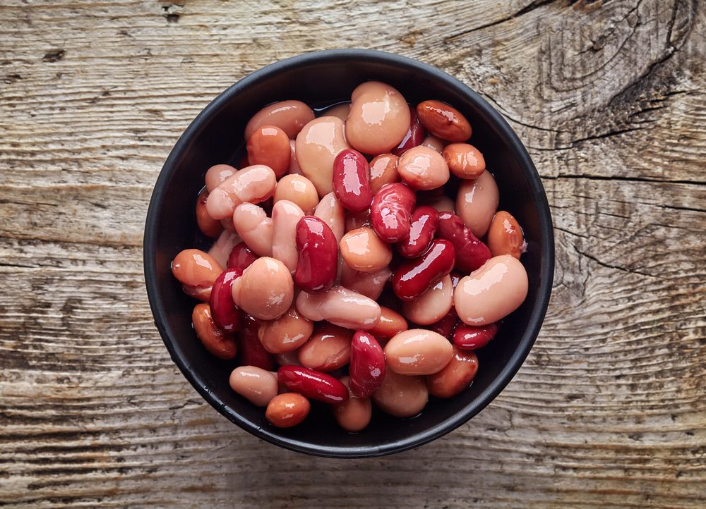 Various types of canned beans in black bowl on wooden table, top view