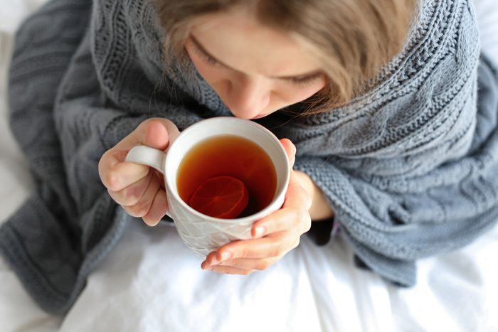 Young ill woman with cup of hot tea at home, closeup