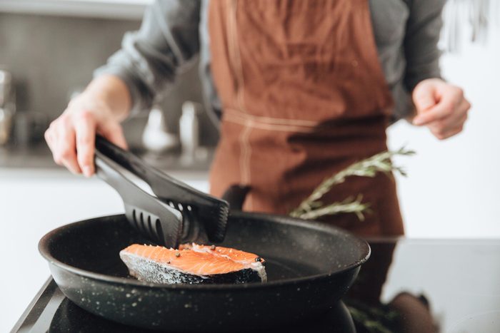 Cropped image of young lady standing in kitchen while cooking salmon.
