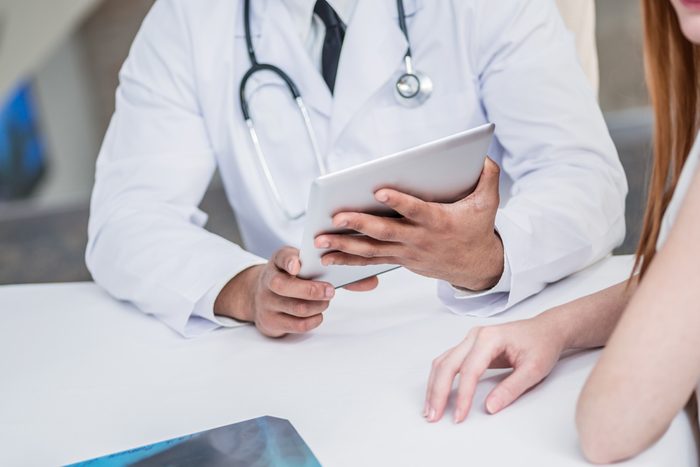 Doctor holding tablet and talking with a patient in the hospital.