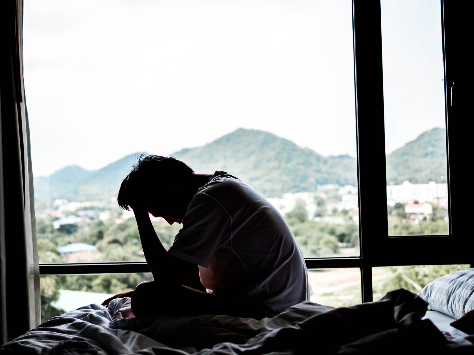 silhouette of a sad man sitting on the bed in the dark