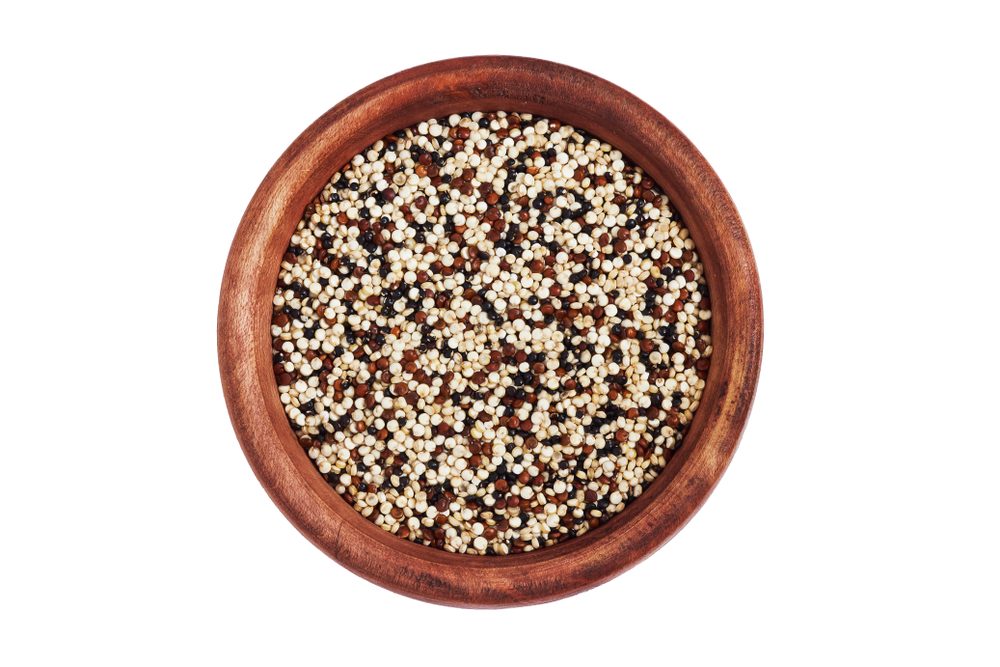 Mixed raw quinoa (Chenopodium quinoa). Red, black and white seeds in wooden bowl isolated on white background