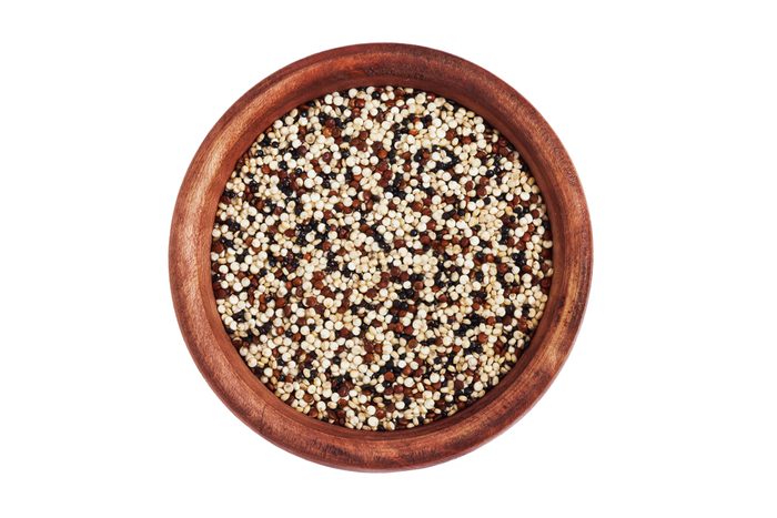 Mixed raw quinoa (Chenopodium quinoa). Red, black and white seeds in wooden bowl isolated on white background