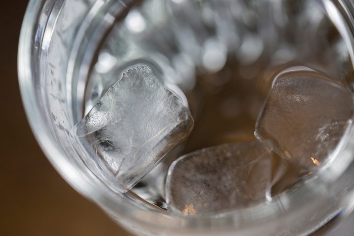 Glass with water and melting ice cubes inside placed on the brown surface. Macro shot from the top.