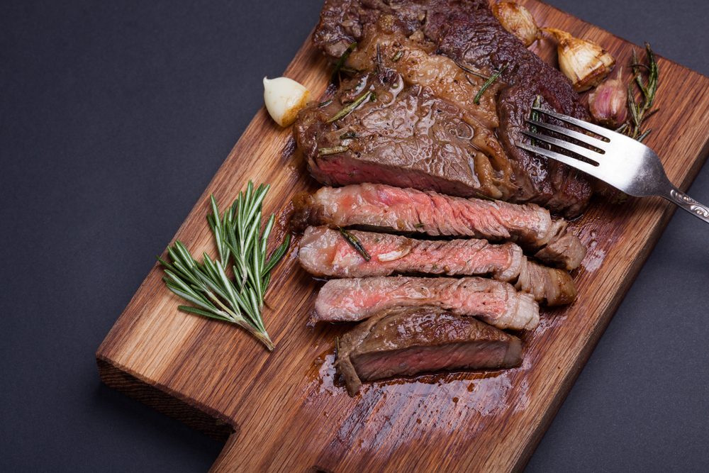 Grilled ribeye steak of marble beef closeup with spices on a wooden Board. Juicy steak medium sliced and ready to eat. Meat cow breed black Angus. With copy space. Top view.