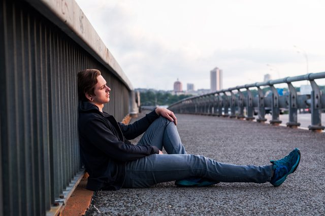 sad young man is sitting near fencing