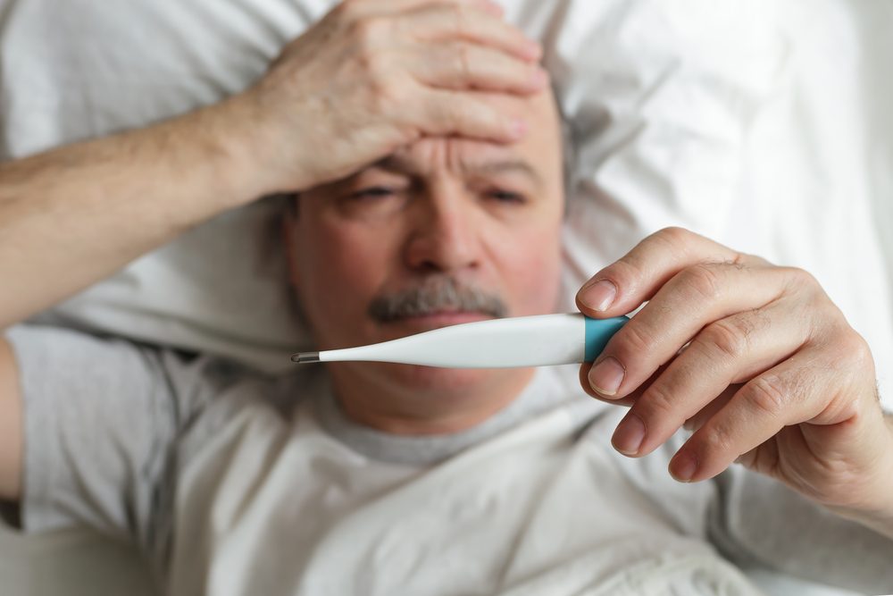 An elderly man measures the temperature with a thermometer. Heat and headache for colds or flu