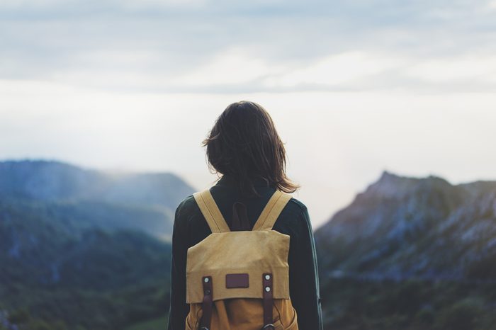 Hipster young girl with bright backpack enjoying sunset on peak of foggy mountain. Tourist traveler on background valley landscape view mockup. Hiker looking sunlight flare in trip Picos de Europa