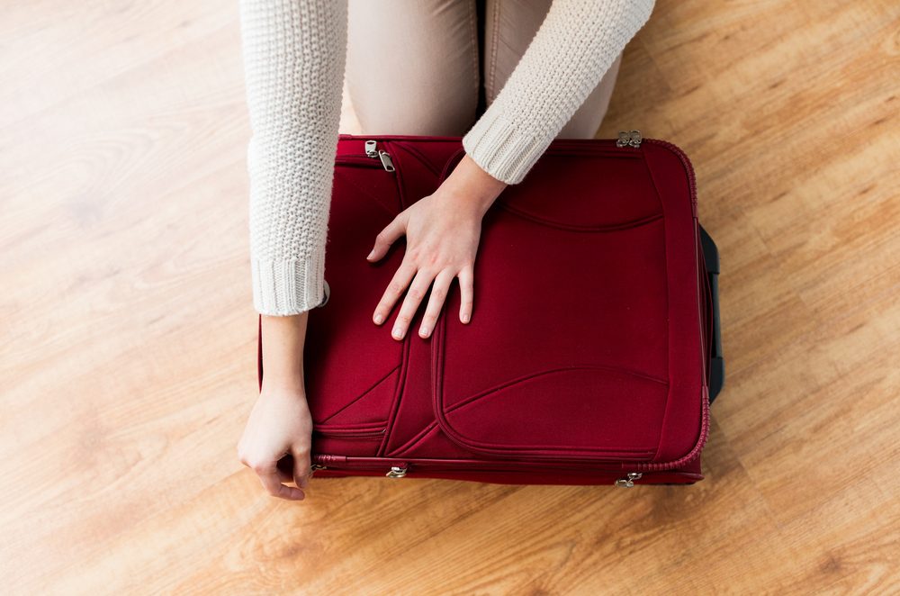 summer vacation, travel, tourism and objects concept - close up of woman packing and zipping travel bag for vacation