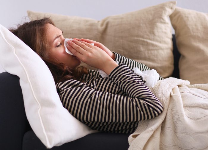 Portrait of a sick woman blowing her nose while sitting on the sofa