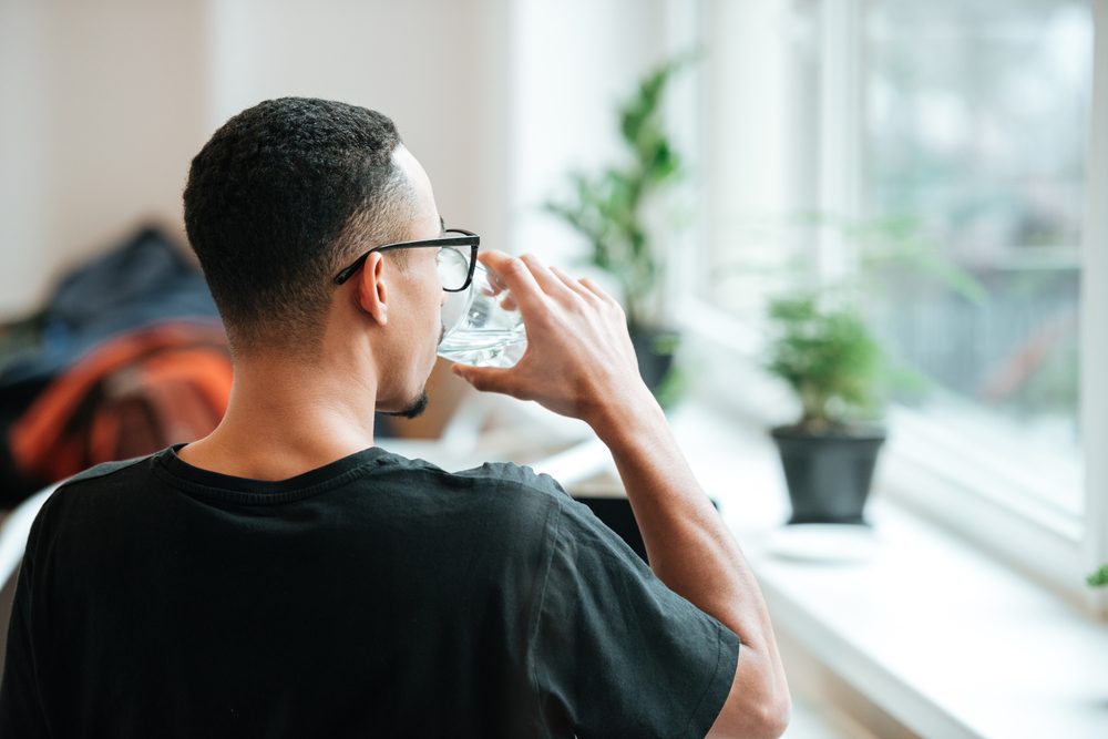 Back view of a young african man drinking water out of glass during coffee break at cafe