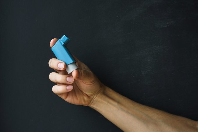 aerosol inhaler for the treatment of asthma in a male hand against a dark background.