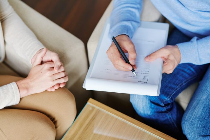 Depressed patient sitting nervously on sofa and explaining her problem to psychologist with clipboard and pen