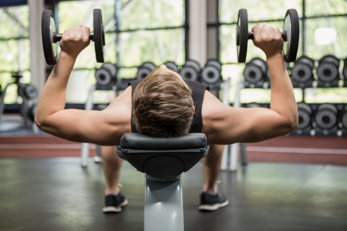 Man lifting dumbbell weights while lying down in gym
