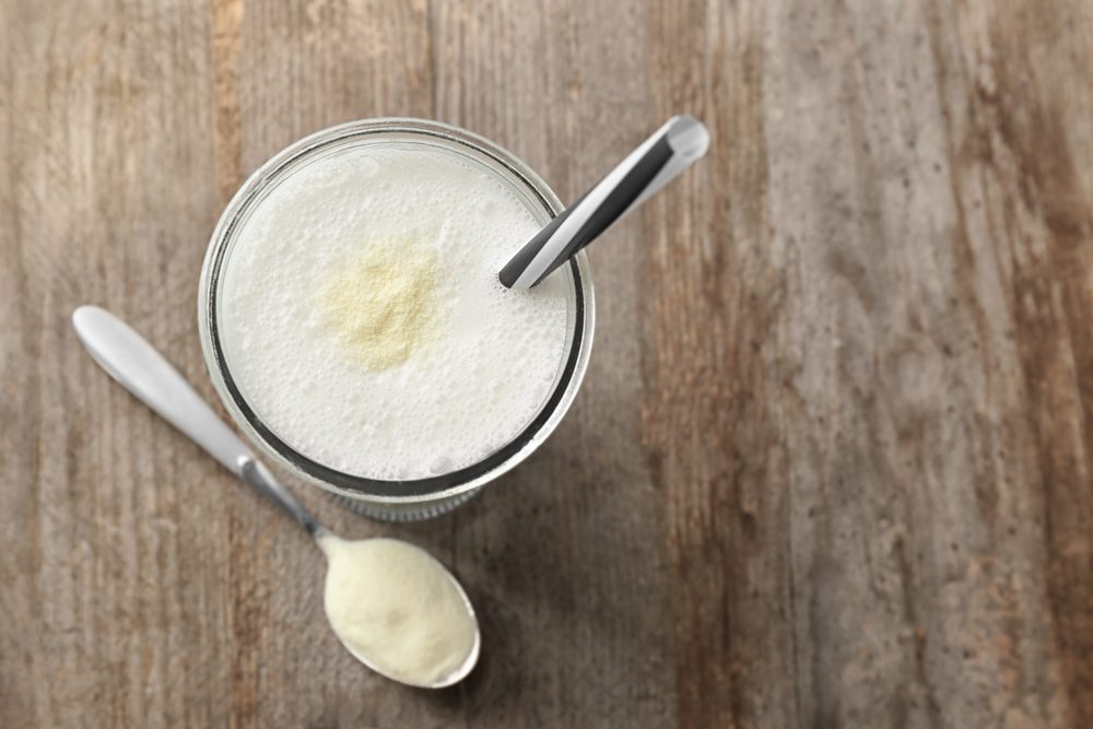 Glass with protein shake and powder in spoon on wooden table