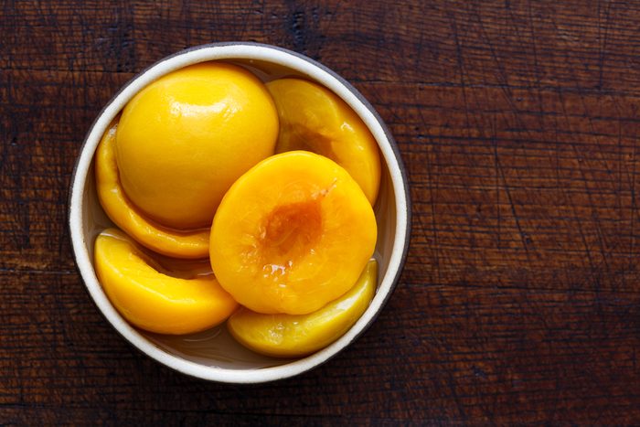 Canned peach halves in bowl isolated on dark background. From above.