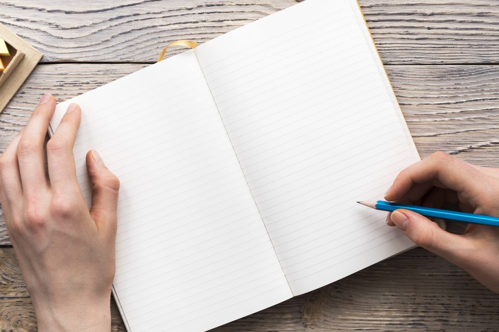 young woman hands hold opened notebook pages with blue pencil in light wooden table with bookmarks