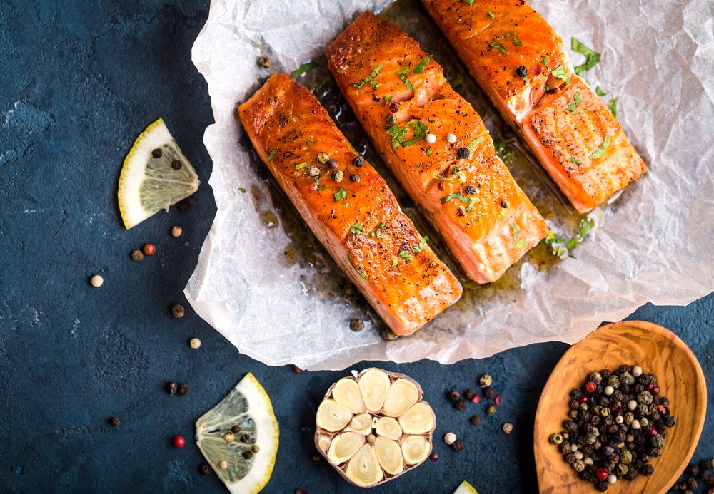 Delicious fried salmon fillet, seasonings on blue rustic concrete background. Cooked salmon steak with pepper, herbs, lemon, garlic, olive oil, spoon. Grilled fish. Fish for healthy dinner. Close-up