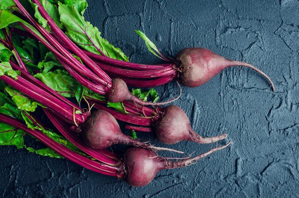 Pile of homegrown organic young beets with green leaves on dark stone table. Fresh harvested beetroots on black concrete background. Top view.