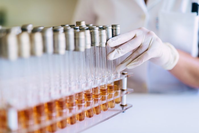 Close up shot of human hand holding white transparent tube with some liquid inside.