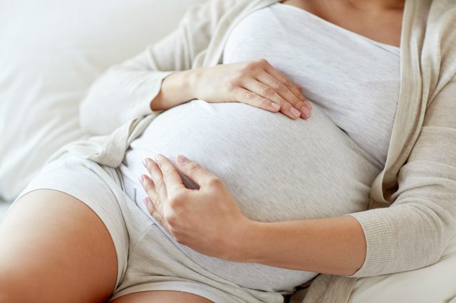 pregnancy, rest, people and expectation concept - close up of pregnant woman lying in bed and touching her belly at home