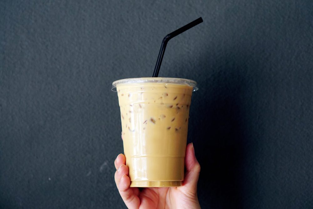 Woman holding plastic glass of iced coffee with milk on grey background