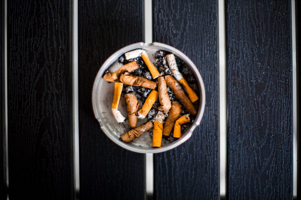 An ashtray with old smoked cigarettes stands on a black table top view, day